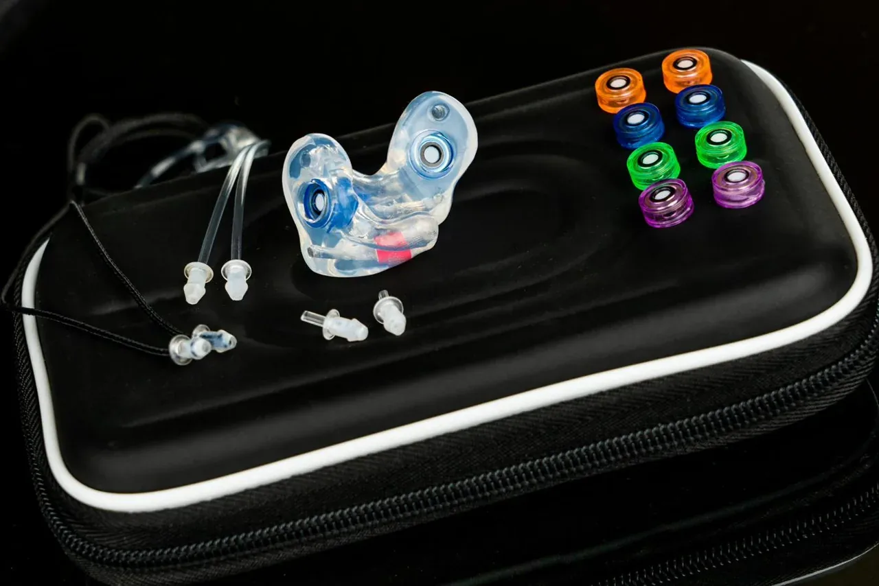 The One filtered custom earplugs, a molded pair shown with the full set of interchangeable colored filters in a zip case